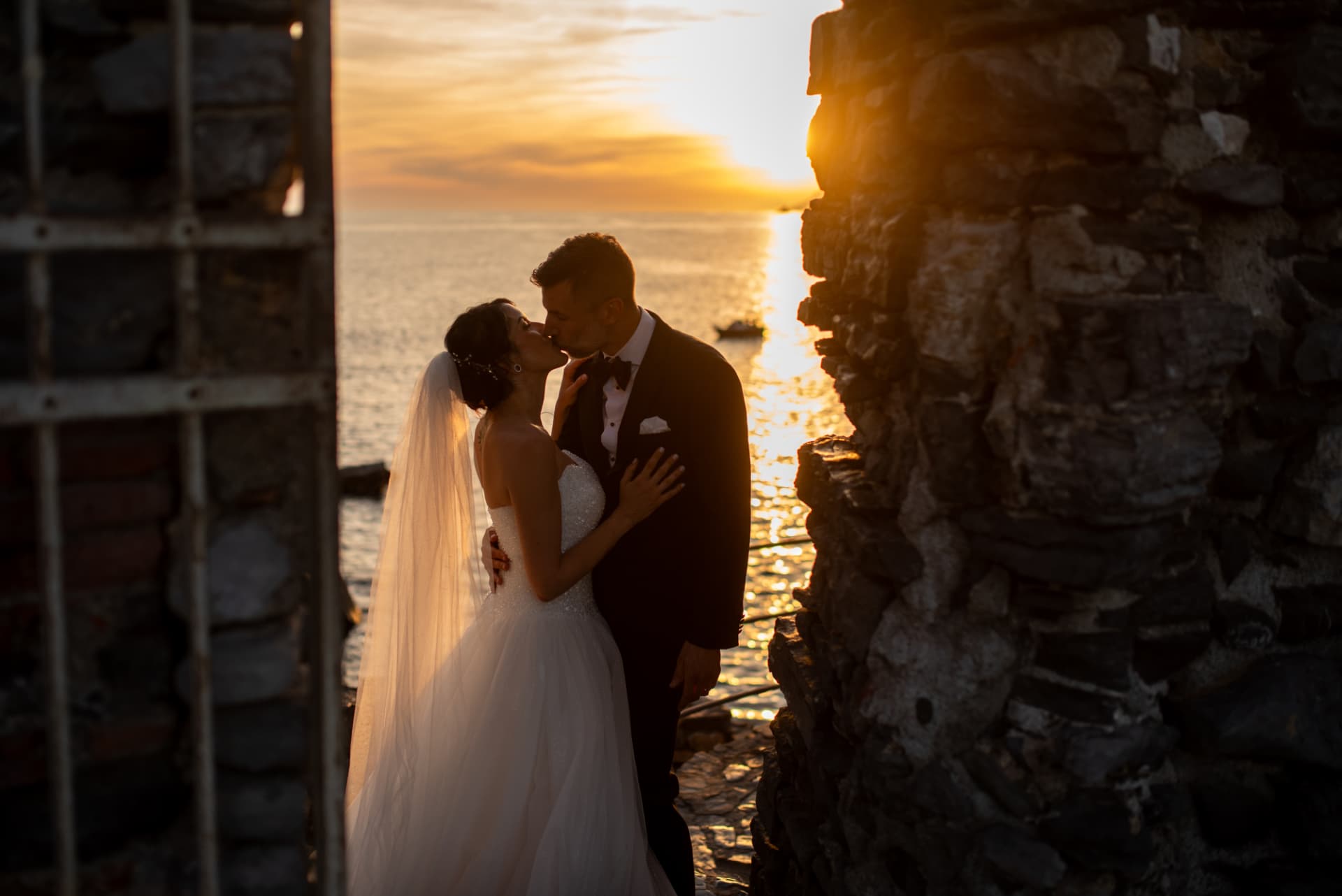 Bacio degli sposi tra le mura in pietra con il sole alle spalle