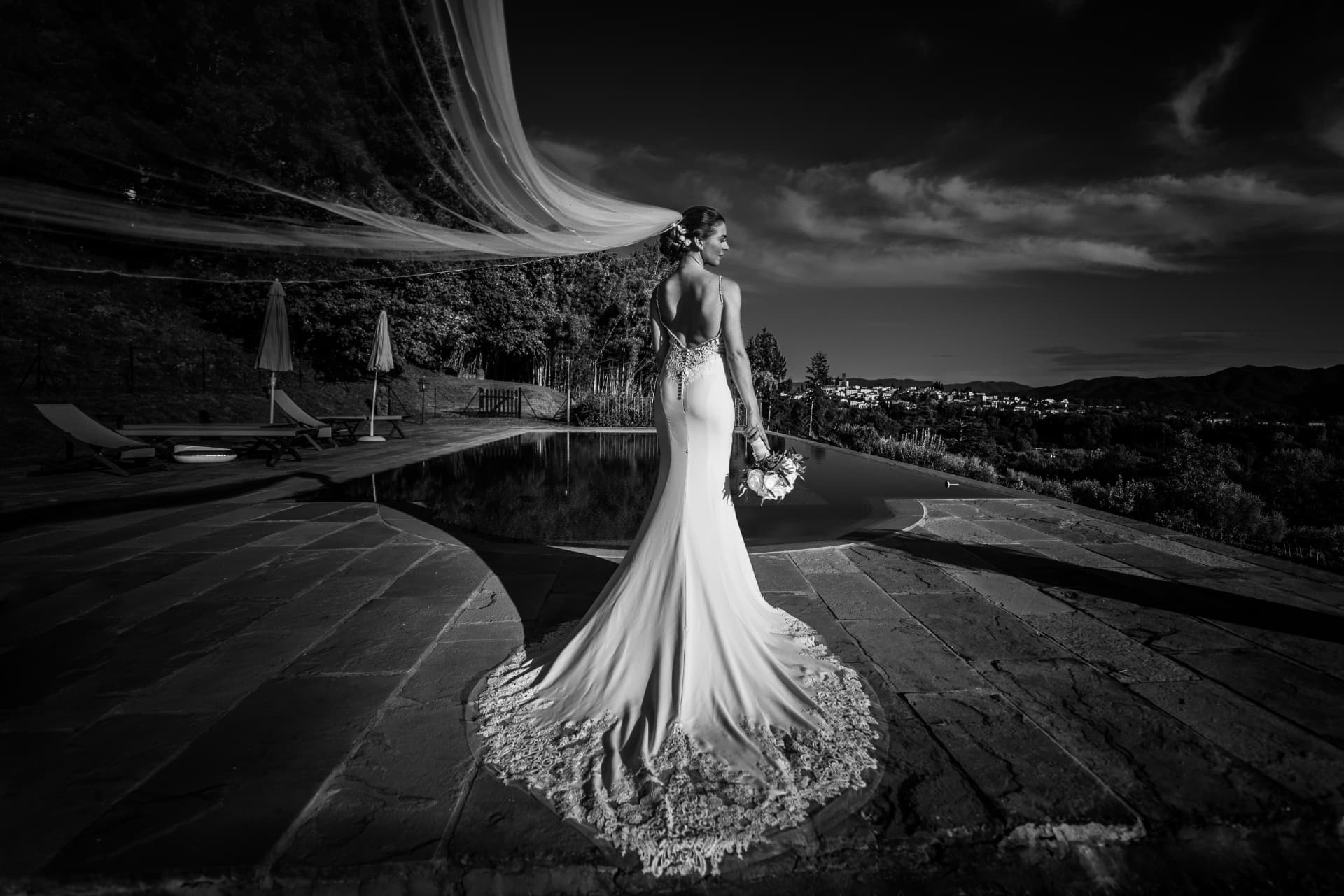 Sposa di spalle con velo mosso dal vento davanti al paesaggio toscano