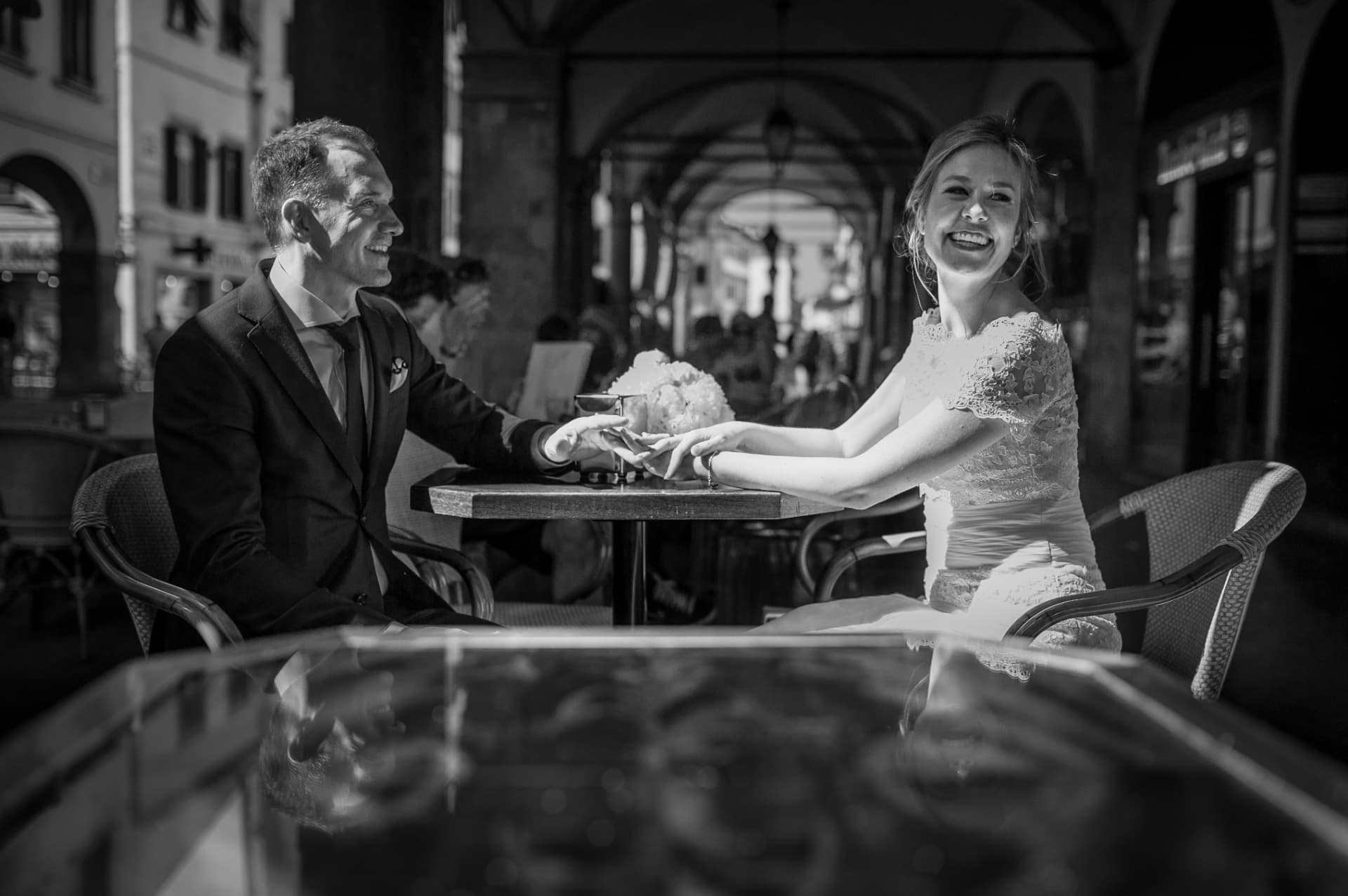 Sposi seduti a un tavolino sotto i portici, mani unite