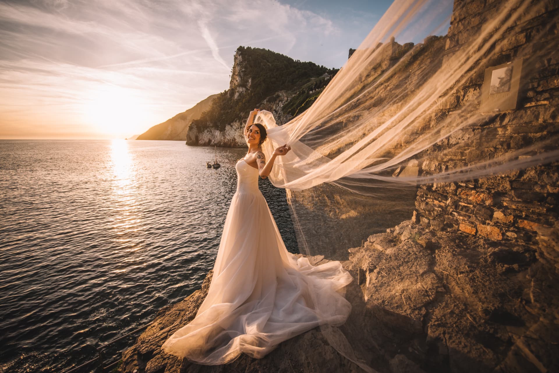 Ritratto della sposa sul mare con il velo sollevato nella luce dorata