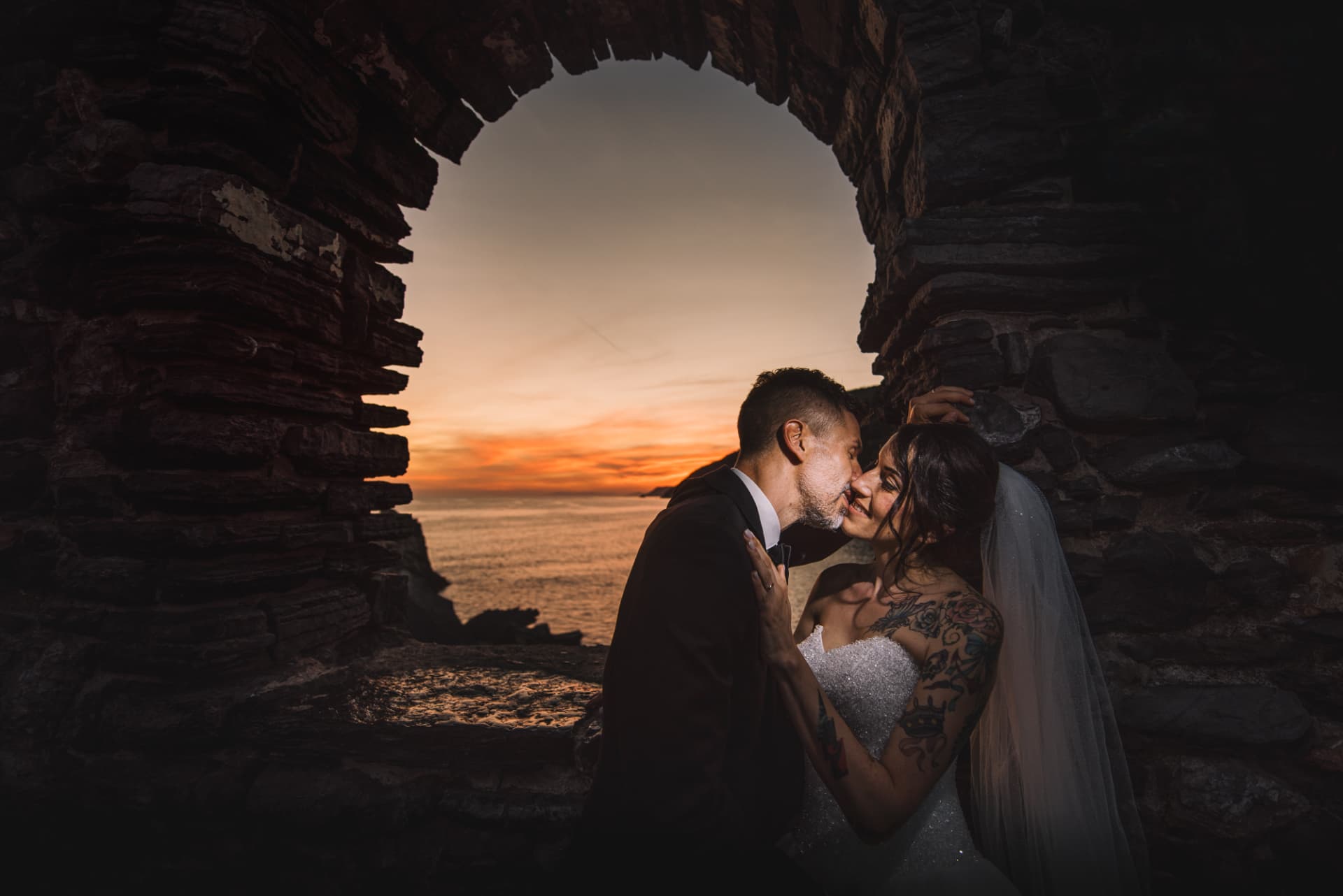 Gli sposi incorniciati dal grande arco in pietra al tramonto