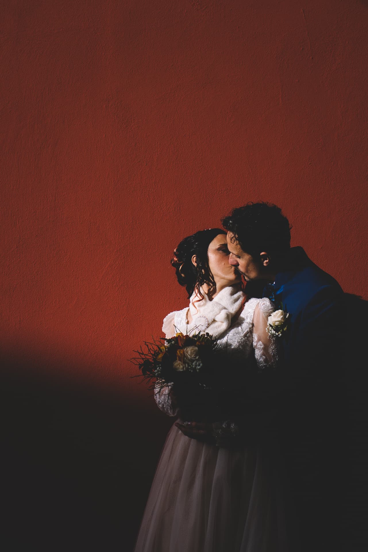 Bacio degli sposi davanti a una grande parete rossa