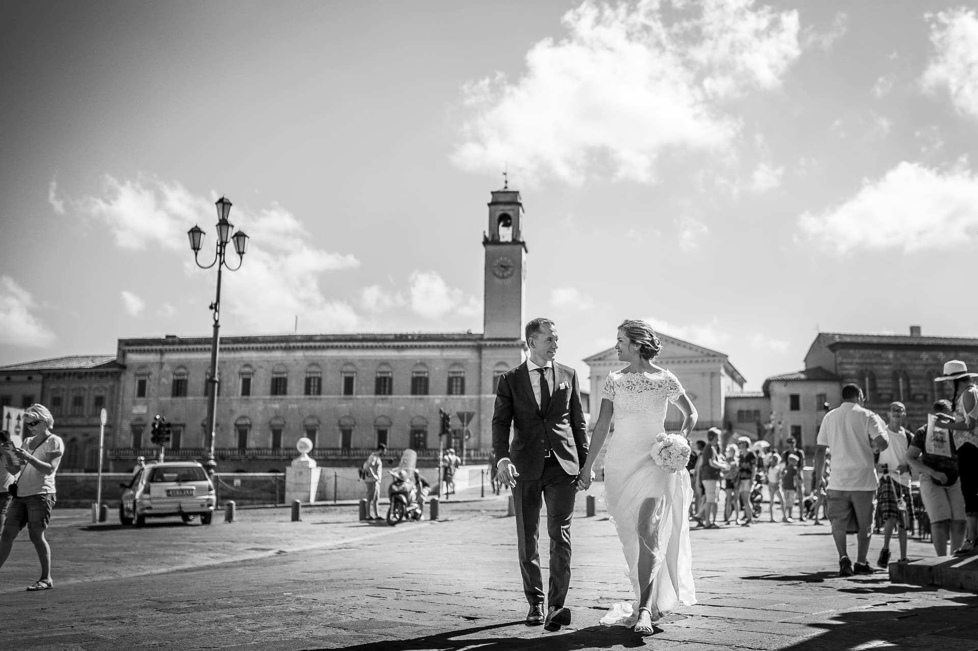 Sposi che attraversano la piazza mano nella mano nella luce del mezzogiorno